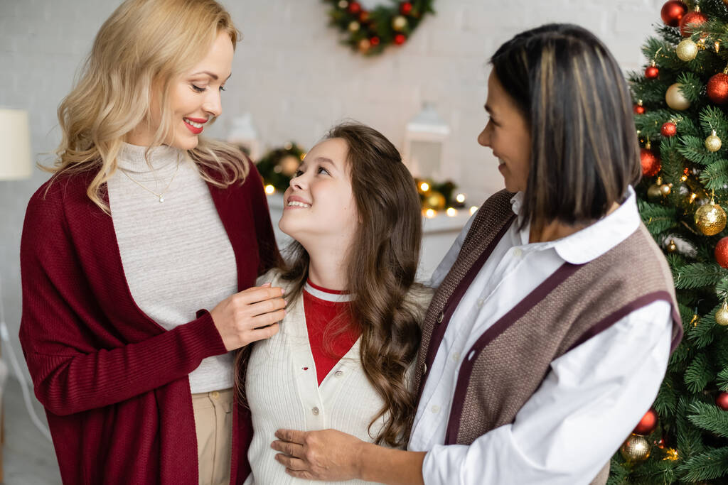 joyful girl looking at smiling mother near multiracial granny and decorated christmas tree - Photo, Image