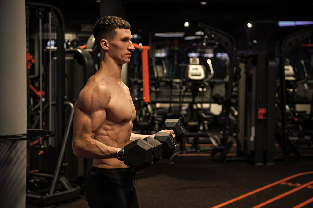 Hombre sin camisa haciendo rizos bíceps tríceps con mancuernas en el gimnasio, entrenamiento de fuerza. - Foto, imagen