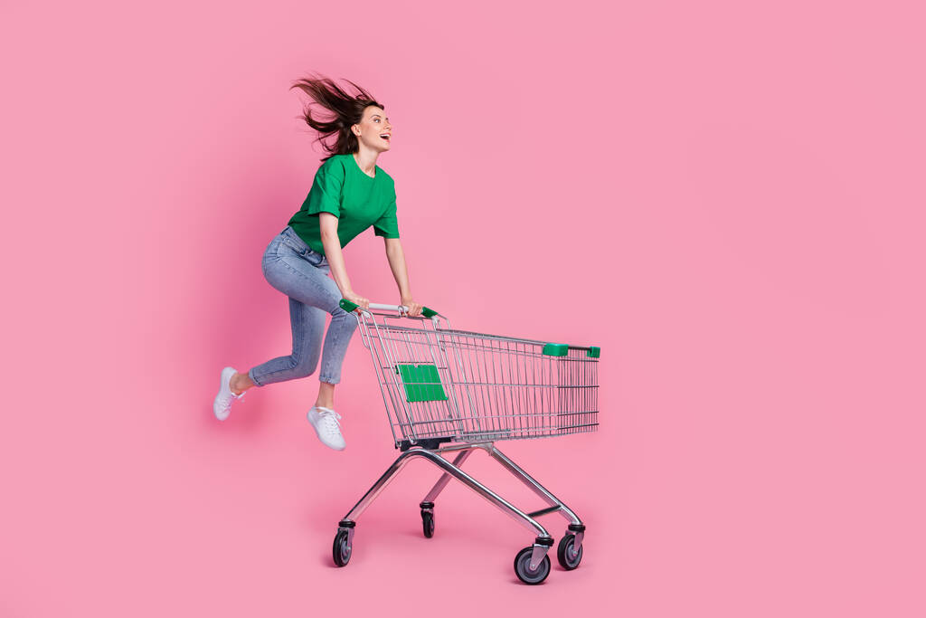 フルサイズの写真の喜び女の子ジャンプラッシュ急いでプッシュスーパーマーケットトロリーピンク色の背景に隔離された. - 写真・画像