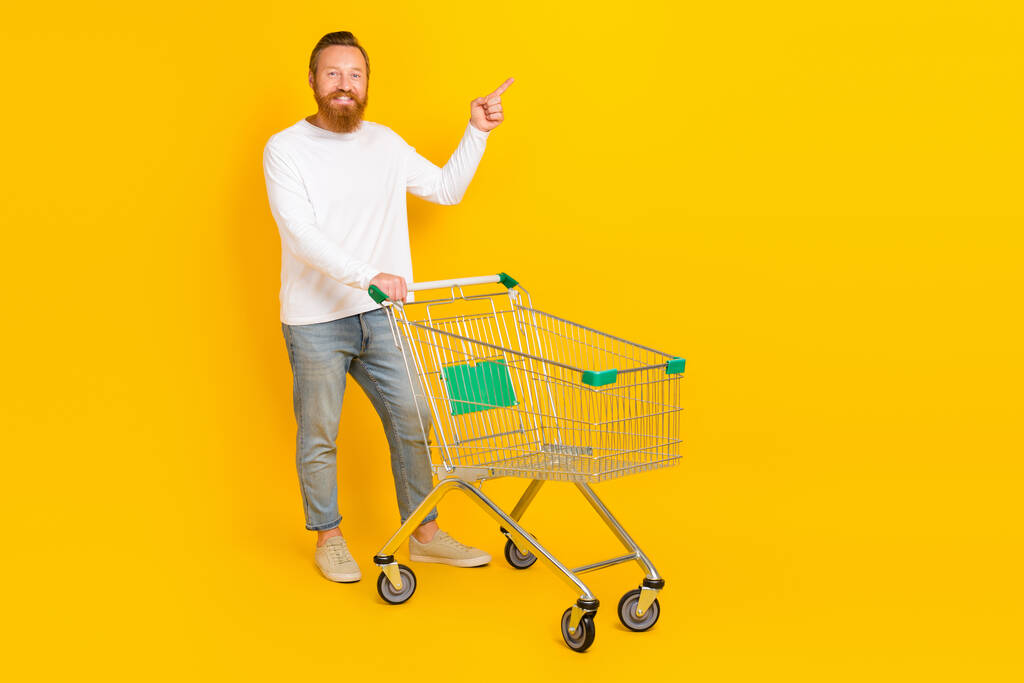 Pełny rozmiar zdjęcie broda człowiek zrobić zakupy wskazują promo nosić białą koszulę dżinsy buty izolowane na żółtym tle kolor. - Zdjęcie, obraz