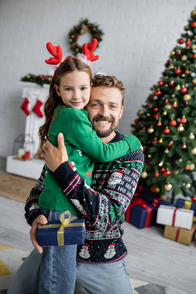 Mosolygó apa átöleli a lányát, és tartja karácsonyi ajándék otthon  - Fotó, kép