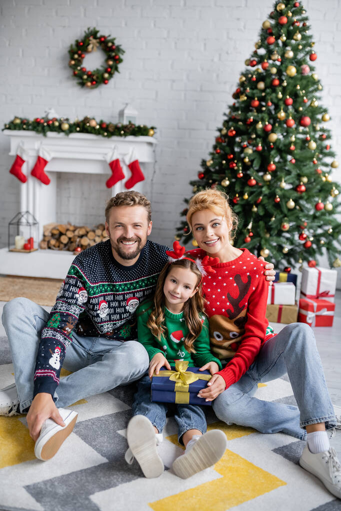 Positif aile, Noel hediyesini evde, şenlikli bir dekorun yanında tutuyor.  - Fotoğraf, Görsel