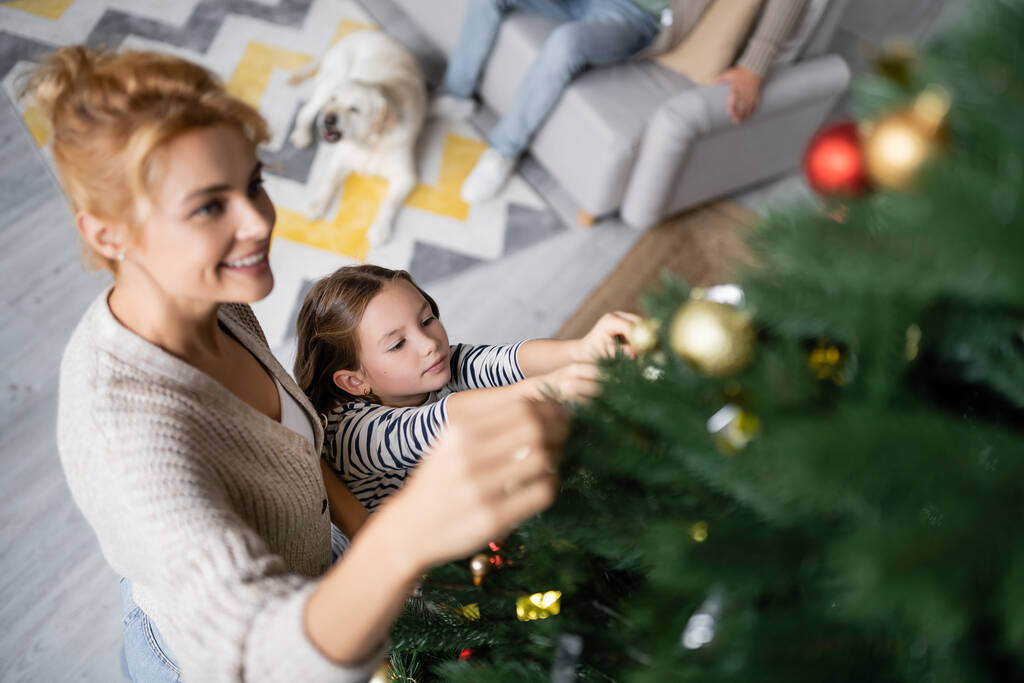 Hohe Blickwinkel von Mädchen schmücken Weihnachtsbaum mit Mama zu Hause  - Foto, Bild