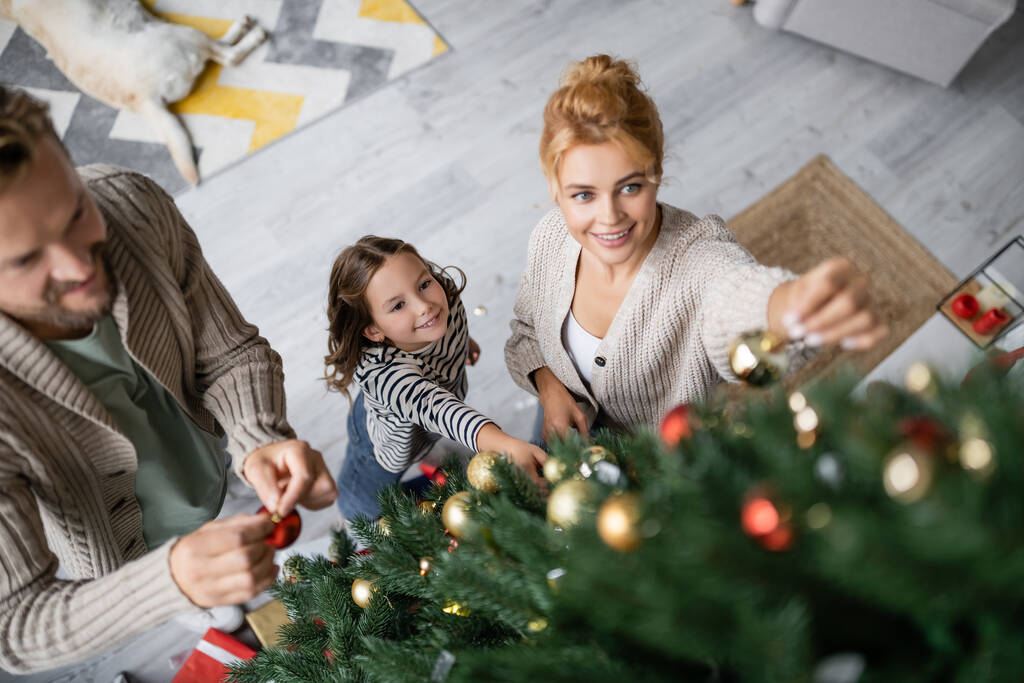 Vista ad alto angolo di famiglia sorridente che tiene le palle vicino all'albero di Natale a casa  - Foto, immagini