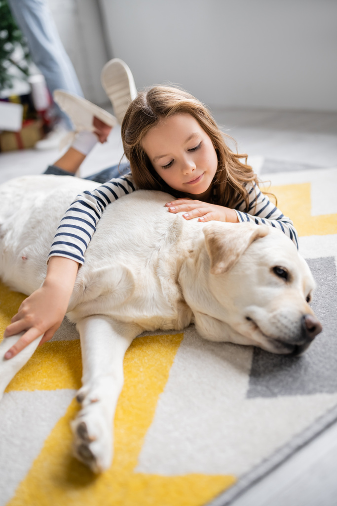 Dívka objímající labrador zatímco ležel na podlaze doma  - Fotografie, Obrázek