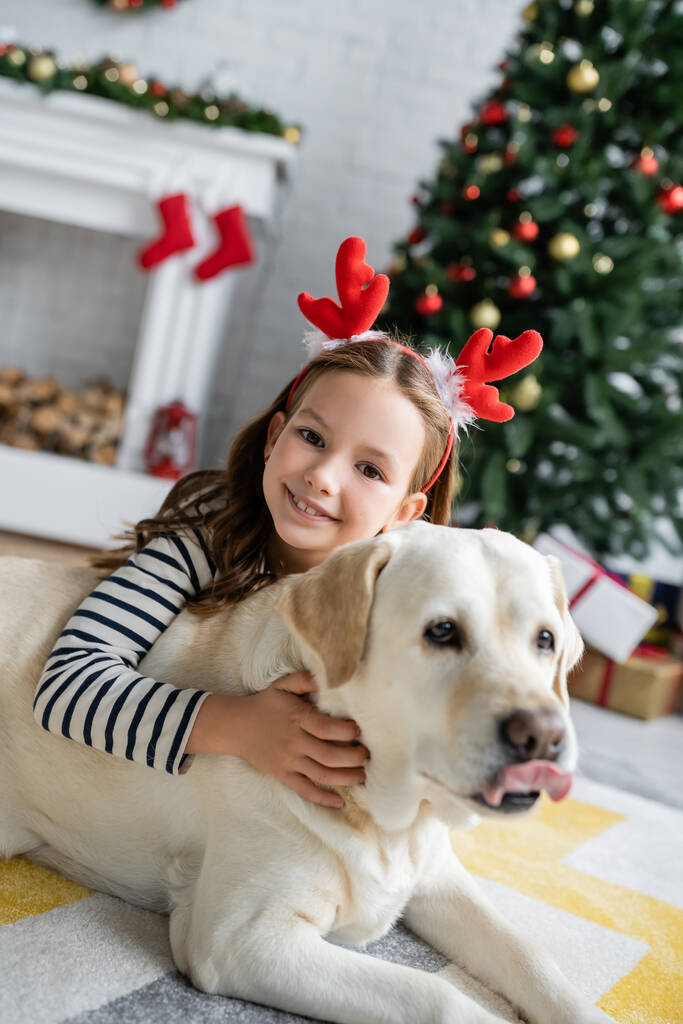 Hymyilevä tyttö jouluna otsanauha silitys labrador kotona  - Valokuva, kuva