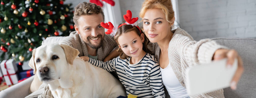 Famille positive avec labrador prendre selfie sur smartphone au cours de la nouvelle année à la maison, bannière  - Photo, image
