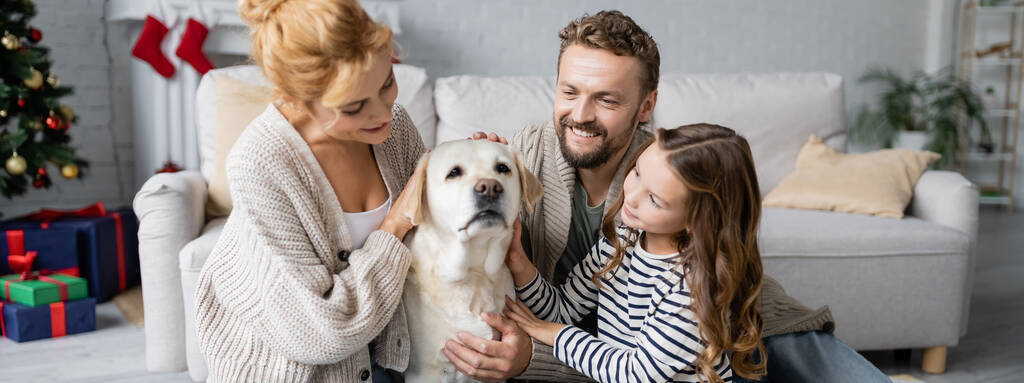 Onnellinen perhe hyväily labrador koira aikana uusi vuosi olohuoneessa, banneri  - Valokuva, kuva