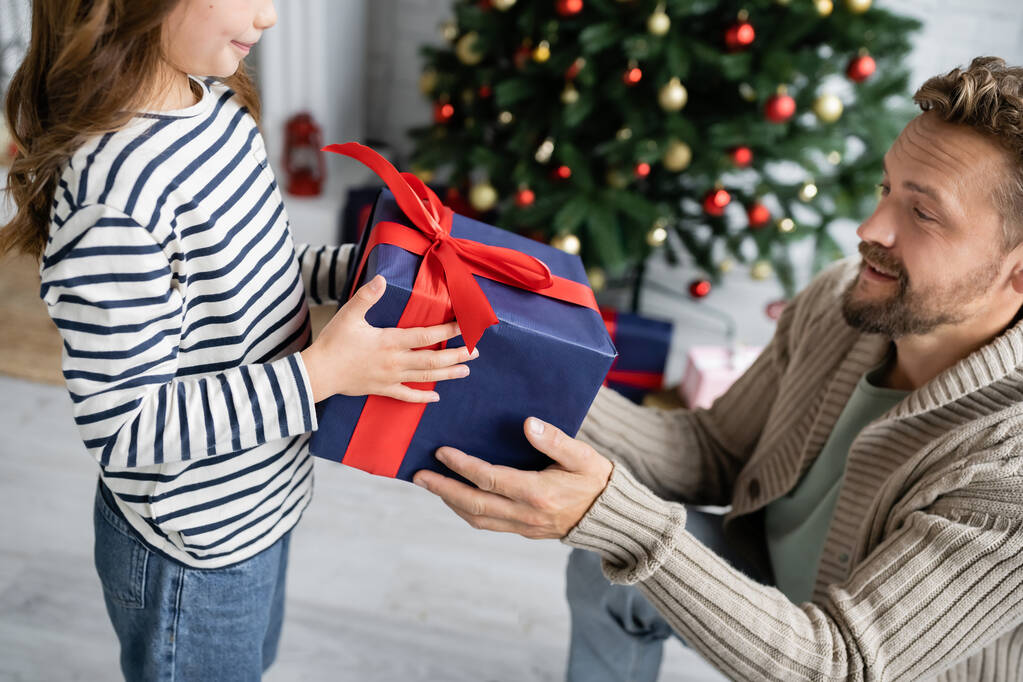 Kid giving new year present to father near blurred christmas tree at home  - Photo, Image