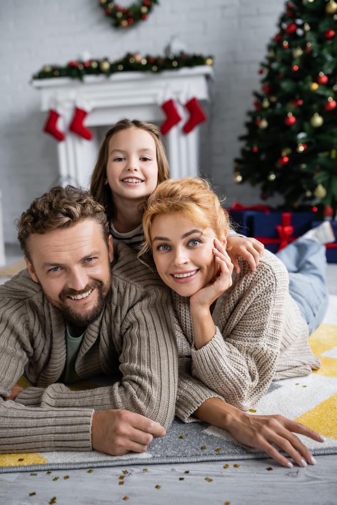 笑顔の家族はカメラを見ながら、新年の間にコンフェッティと床に横たわっています  - 写真・画像