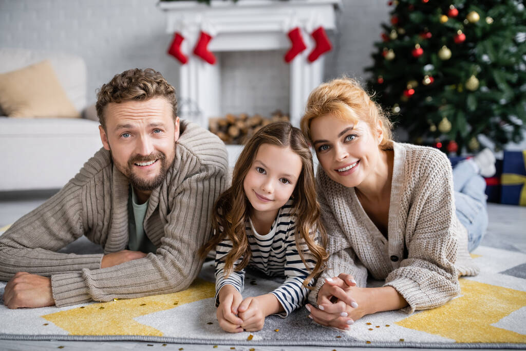 正の家族と子供は家で新年の間にカーペットの上でコンフェッティの近くに横たわっています  - 写真・画像