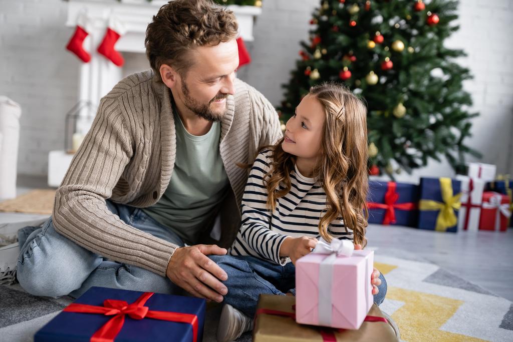 Hymyilevä mies halaus tytär lähellä joululahjoja kotona  - Valokuva, kuva