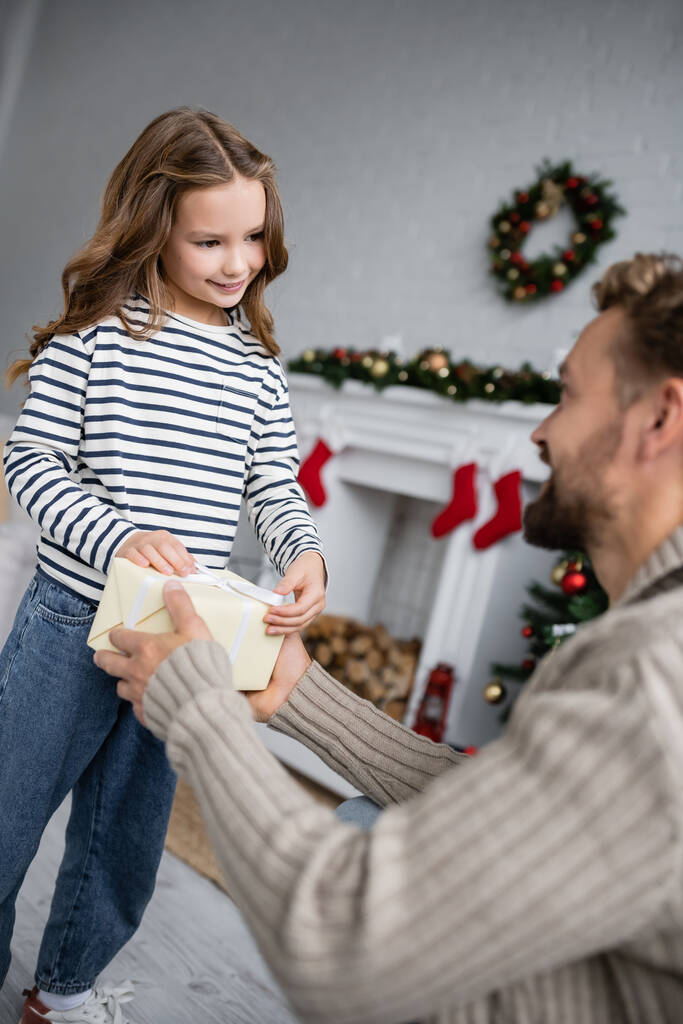 Размытый мужчина дарит рождественский подарок улыбающейся дочери дома  - Фото, изображение