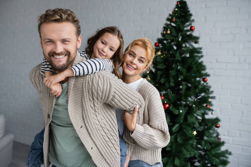 Ευτυχισμένη οικογένεια αγκαλιάζει και κοιτάζοντας κάμερα κατά τη διάρκεια των Χριστουγέννων γιορτή στο σπίτι  - Φωτογραφία, εικόνα