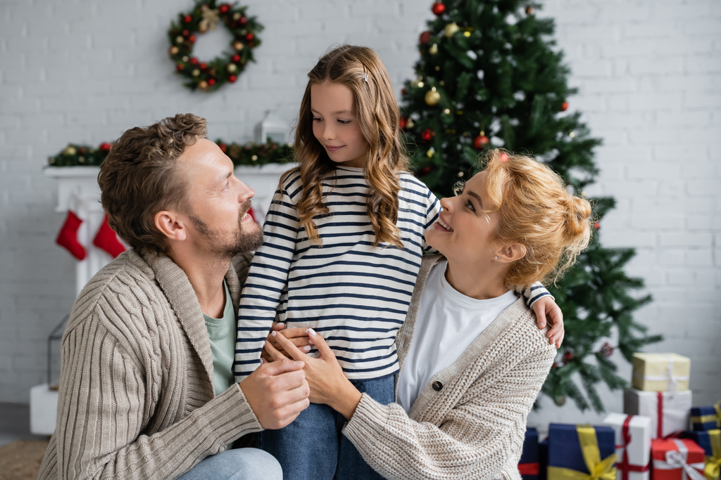 Usmívající se rodiče v svetrech při pohledu na dceru během vánoc doma  - Fotografie, Obrázek