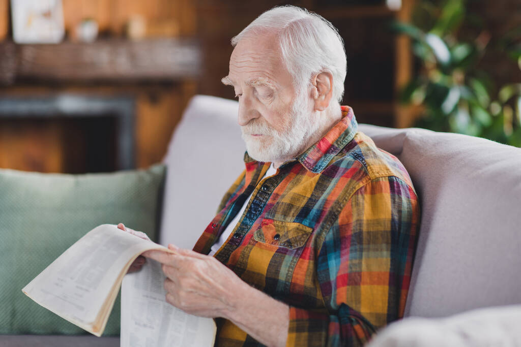 Photo of calm peaceful grandparent white hair relaxing reading article newspaper dressed casual plaid clothes sit couch indoors flat room. - Photo, Image