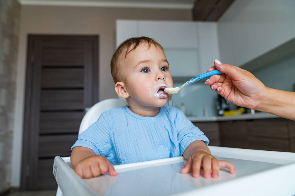 かわいい赤ちゃんの男の子はスプーンでお粥を食べる。かわいい顔の練習を食べる男の子. - 写真・画像