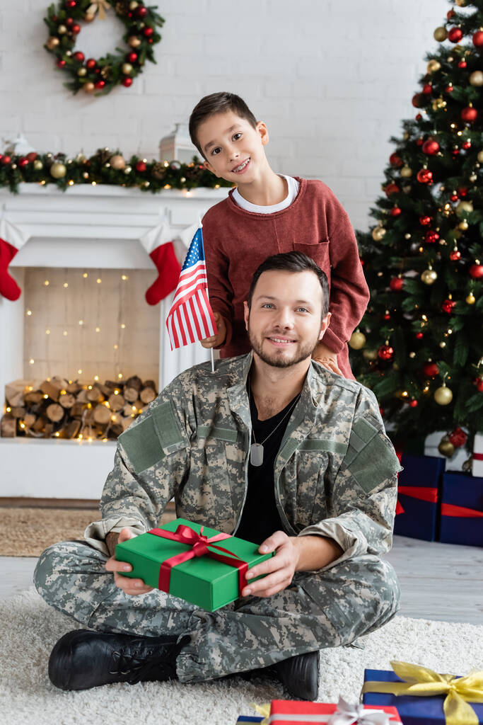 boldog fiú amerikai zászló és katonai férfi karácsonyi jelen nézi kamera otthon - Fotó, kép