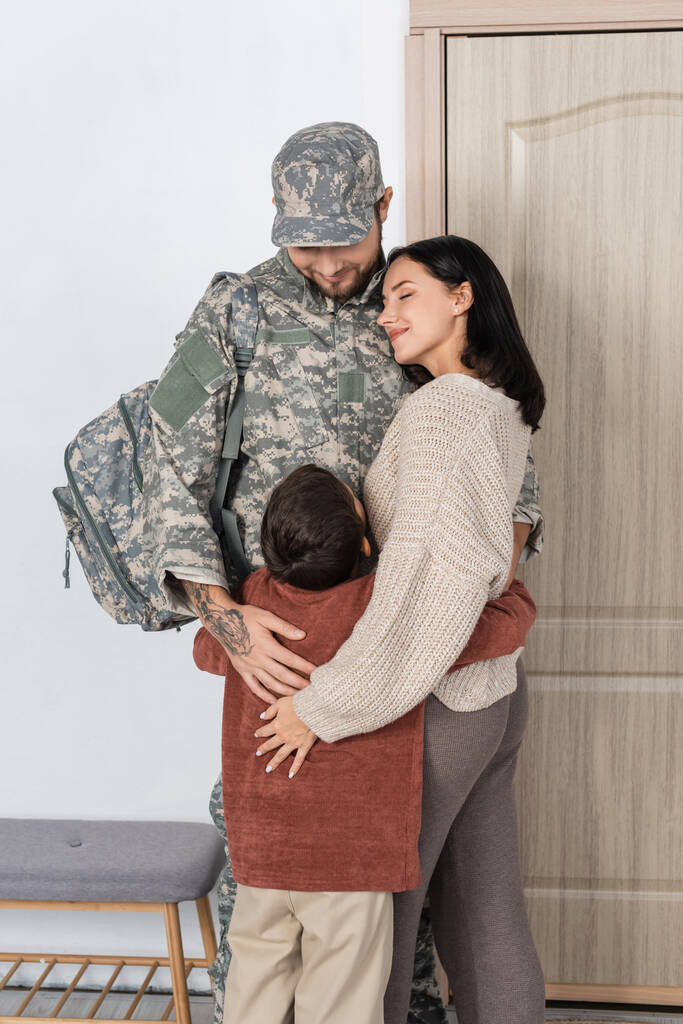 Glückliche Mutter und Kind umarmen Mann in Militäruniform bei seiner Rückkehr nach Hause - Foto, Bild