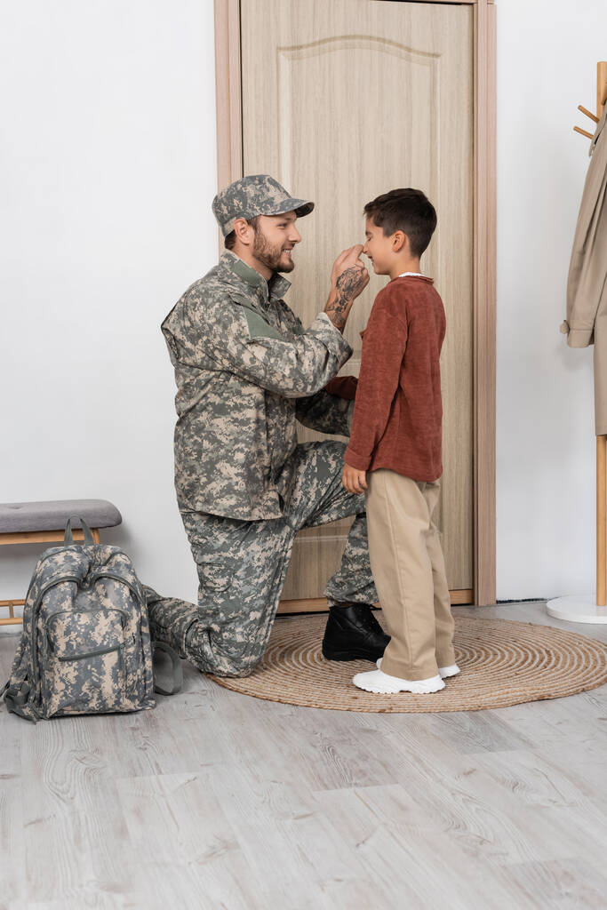 gelukkig man in camouflage aanraken neus van zoon ontmoeten hem in de buurt deur thuis - Foto, afbeelding