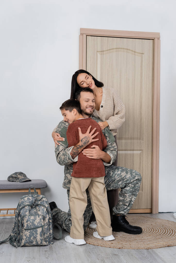 Ευτυχισμένη οικογένεια που αγκαλιάζει έναν ευτυχισμένο στρατιωτικό που επιστρέφει σπίτι - Φωτογραφία, εικόνα