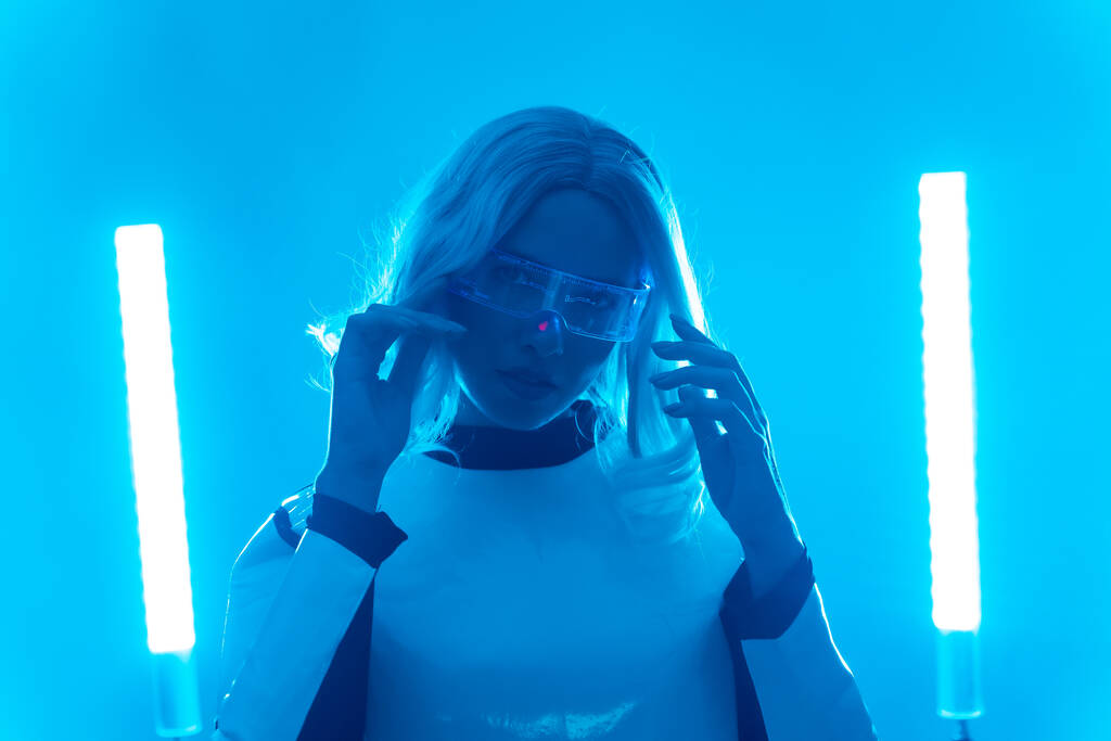 Žena v futuristickém obleku a brýlích s modrými světly, virtuální nebo metaverzní koncepcí, dívající se do kamery - Fotografie, Obrázek
