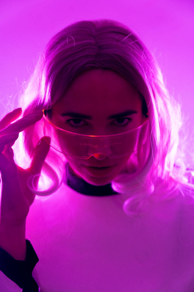 Una mujer en un traje futurista y gafas con luces rosadas, concepto virtual o metaverso - Foto, imagen
