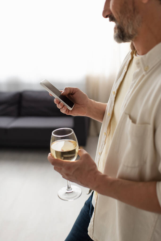 bijgesneden weergave van wazige man met glas witte wijn met behulp van smartphone met leeg scherm - Foto, afbeelding