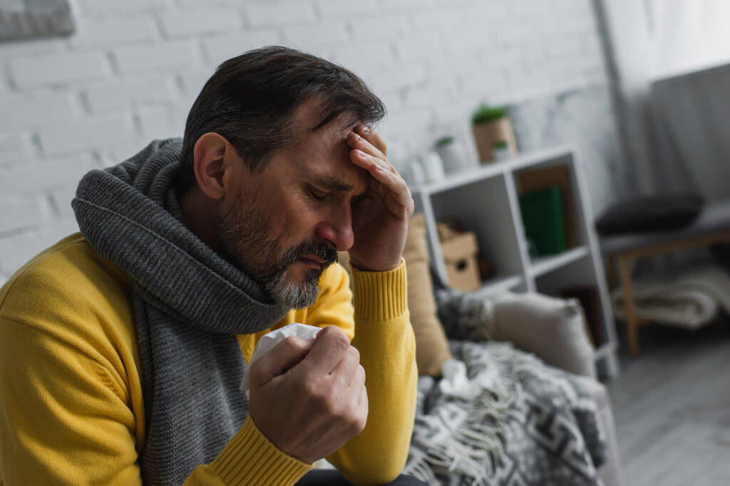 diseased man in warm scarf holding paper napkin and suffering from headache  - Photo, Image
