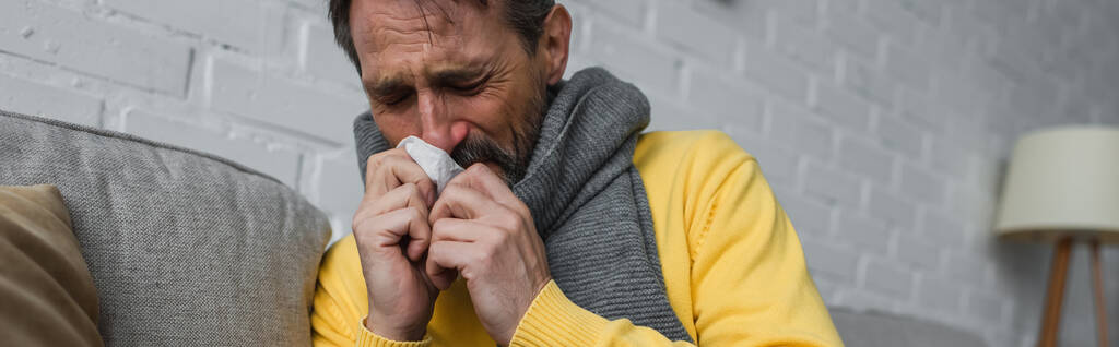 uomo malato in sciarpa calda che soffre di naso che cola e starnuti in tovagliolo di carta, banner - Foto, immagini