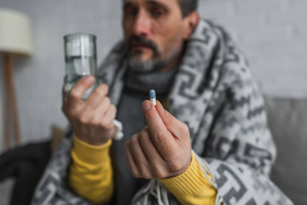 hombre enfermo sosteniendo píldora y vaso de agua sobre fondo borroso - Foto, imagen