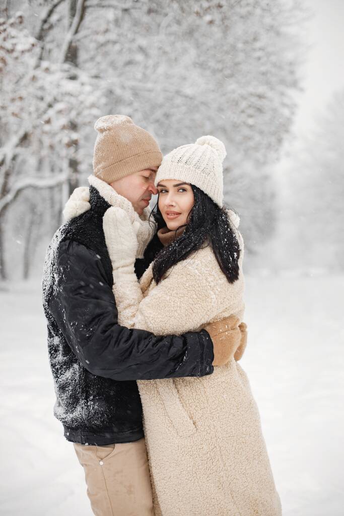 Jeune homme et femme embrassant et embrassant à l'extérieur. Couple romantique en hiver dans des vestes chaudes marcher dans le parc et câlins. Homme et femme vêtus de vêtements d'hiver et chapeaux tricotés. - Photo, image