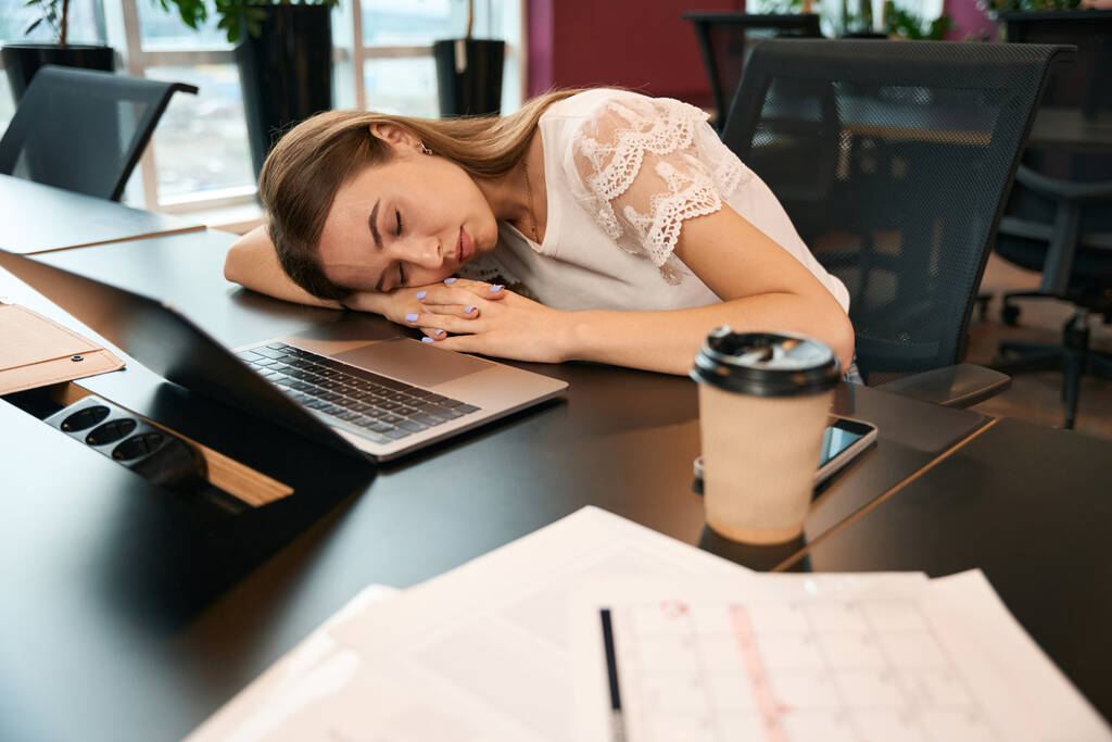 Trabajadora de oficina cansada durmiendo en el escritorio antes de la computadora portátil durante el descanso del café - Foto, imagen