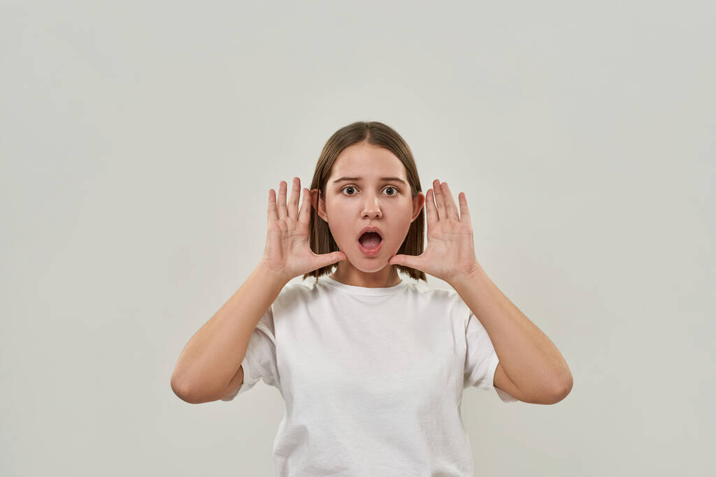 Потрясенная кавказская девочка-подросток с открытым ртом смотрит в камеру. Женщина поколения зумеров в футболке. Концепция современного молодого образа жизни. Изолирован на белом фоне в студии. Копирование пространства - Фото, изображение