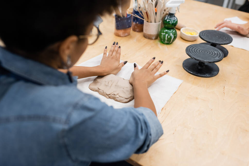 vysoký úhel pohledu na kudrnaté africké americké ženy v brýlích tvarování hliněný kus s rukama během keramiky třídy - Fotografie, Obrázek