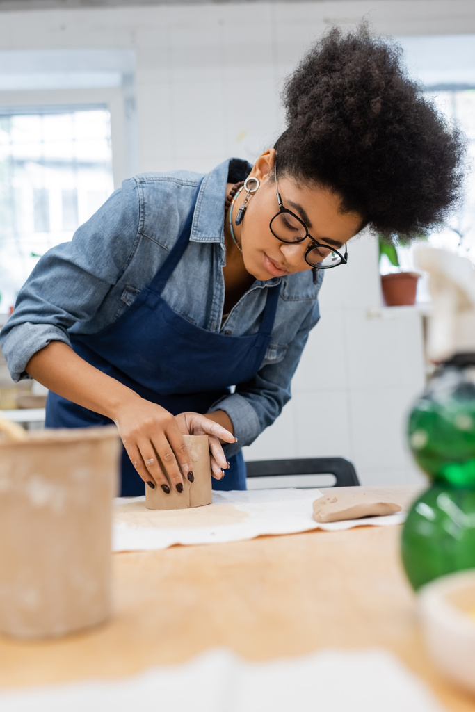 mladá africká americká žena v zástěře modelování hliněný kus během keramiky třídy  - Fotografie, Obrázek