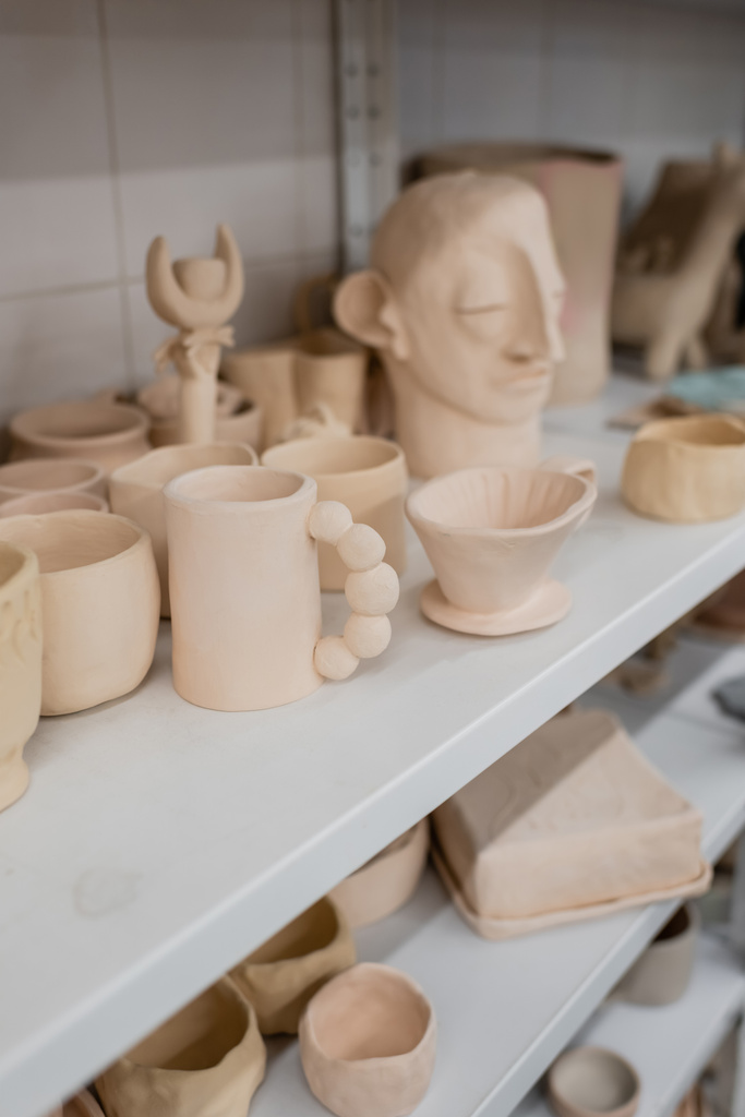 различные глиняные скульптуры возле кубков на полках керамического магазина  - Фото, изображение
