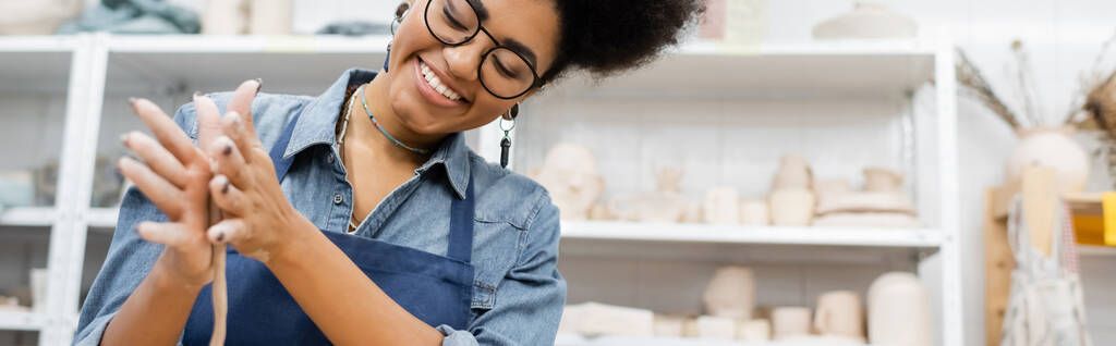 Artigiana afroamericana positiva in grembiule che forma argilla in laboratorio, banner  - Foto, immagini