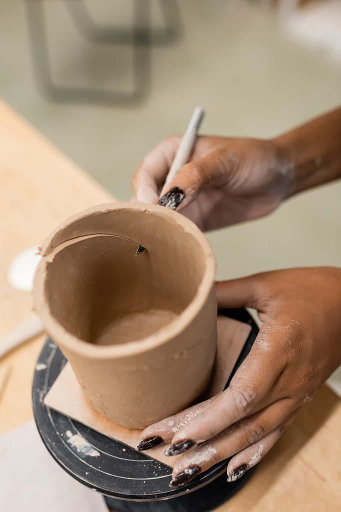 Vista recortada de la artesana afroamericana cortando arcilla en taller de cerámica  - Foto, imagen