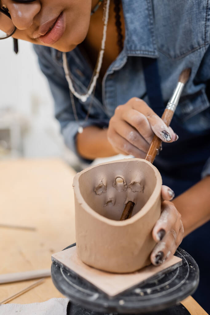 Ausgeschnittene Ansicht einer afrikanisch-amerikanischen Kunsthandwerkerin, die in einer Töpferei an Tonprodukten arbeitet  - Foto, Bild