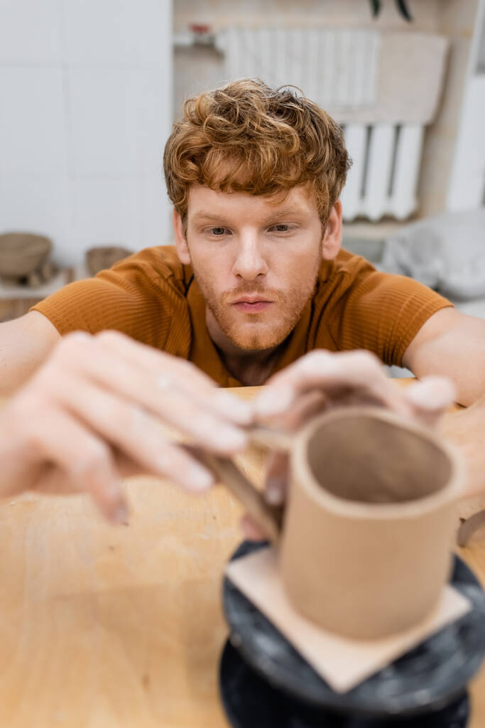 Pelirroja artesanal haciendo taza de arcilla borrosa en taller de cerámica  - Foto, imagen