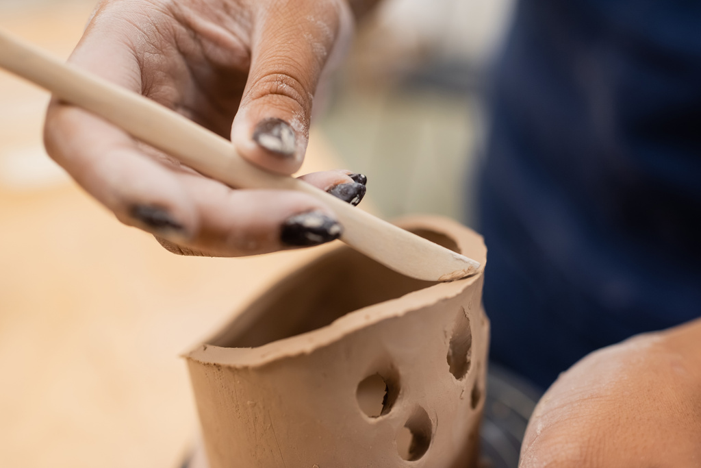 Vista de cerca de la artesana afroamericana usando herramienta mientras hace producto de arcilla en taller  - Foto, imagen