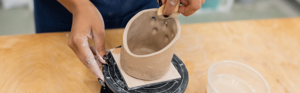Обрезанный вид африканского американского мастера, формирующего глину с губкой в мастерской керамики, баннер  - Фото, изображение