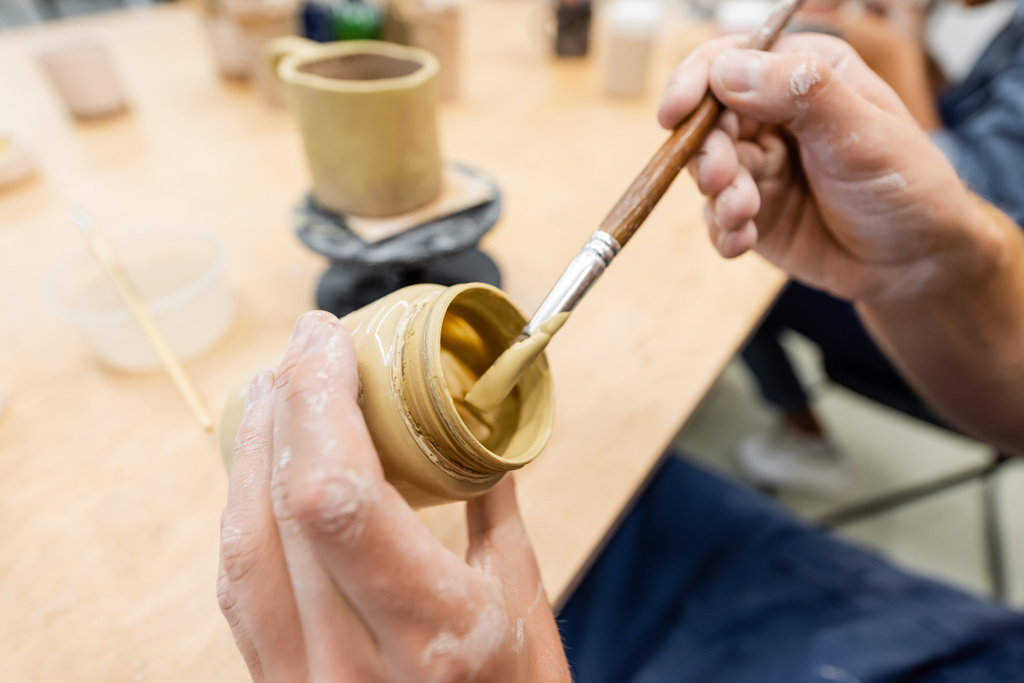 Vista recortada del hombre sosteniendo pincel y pintura en el estudio de cerámica  - Foto, Imagen