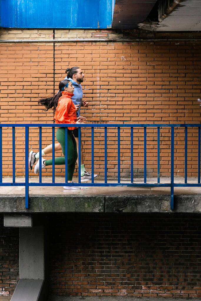 Young woman and her friend wearing sports clothes running in the city during rainy day. - Photo, Image