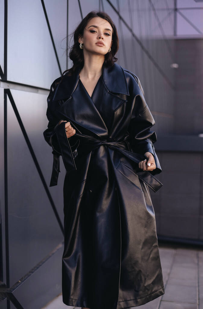 photo extérieure de mode de belle femme aux cheveux foncés dans un élégant manteau en cuir - Photo, image