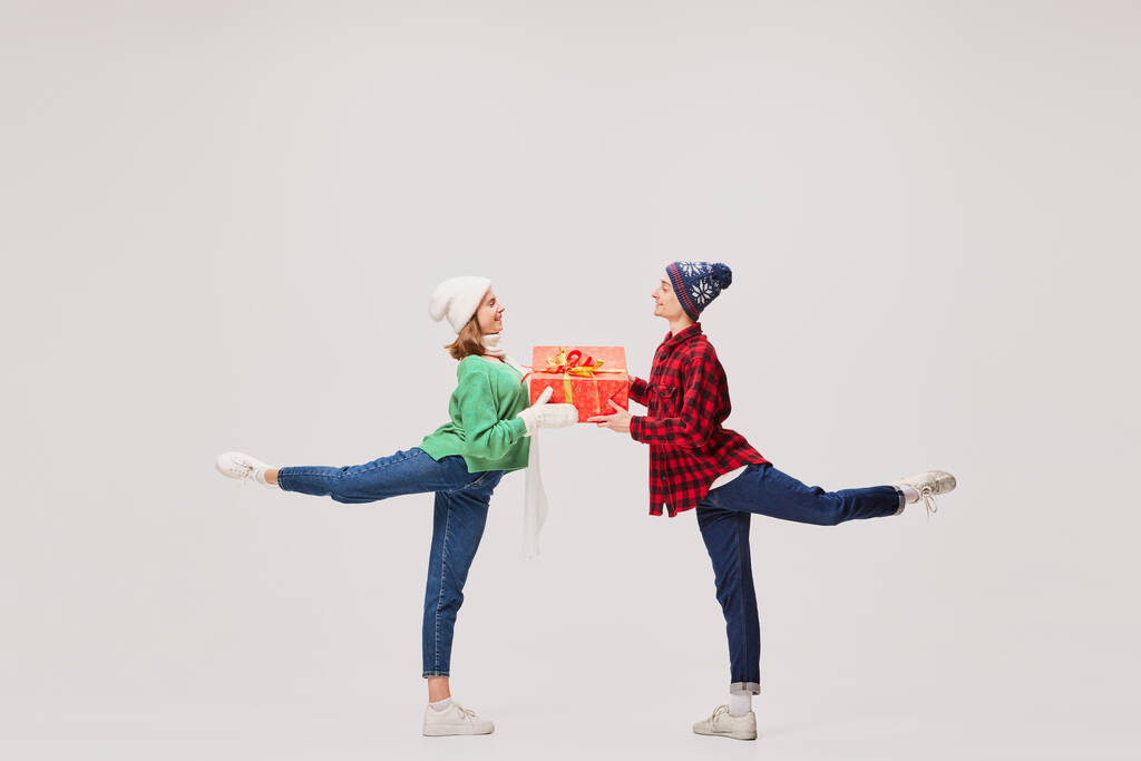 L'amour. Jeunes gens émotionnels, danseurs de ballet en vêtements chauds en action, mouvement avec des boîtes-cadeaux festives lumineuses sur fond gris. Joyeux Noël, Nouvel An, Fêtes, 2023, concept de fête - Photo, image