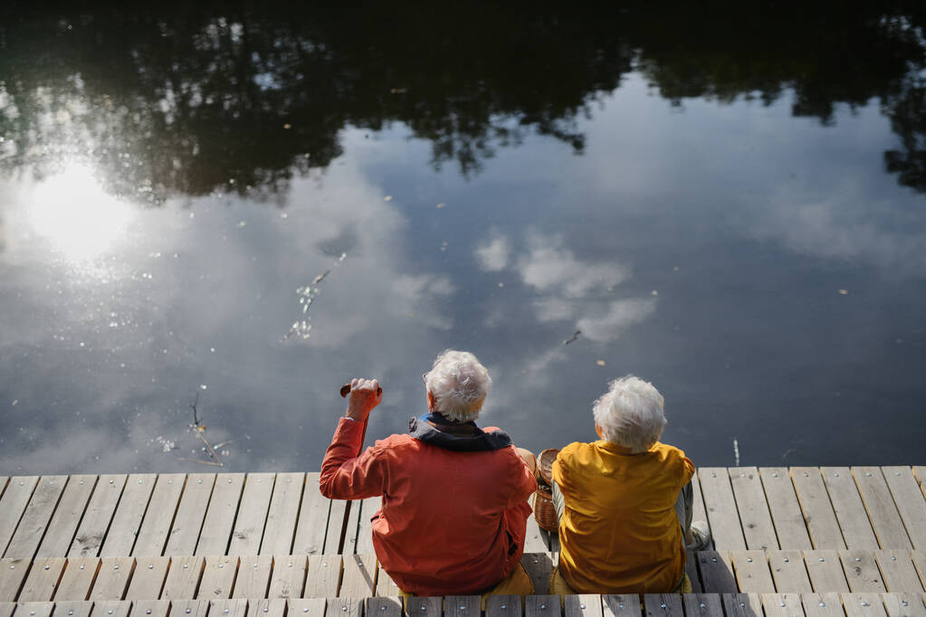 Boldog idős pár ősszel séta a tó mellett, miután szünet, ül a mólón. - Fotó, kép