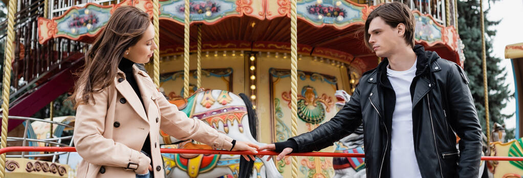 young couple standing near carousel and touching hands in amusement park, banner - Photo, Image