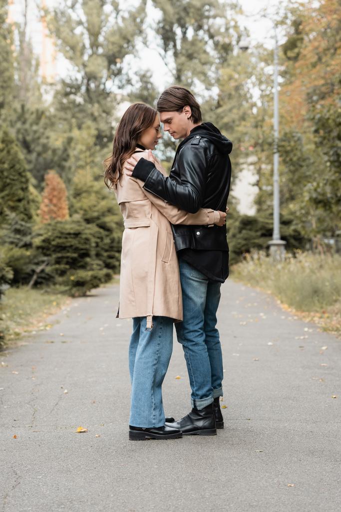 повнометражний вид на стильний молодий чоловік обіймає красиву дівчину в траншеї пальто на відкритому повітрі
 - Фото, зображення